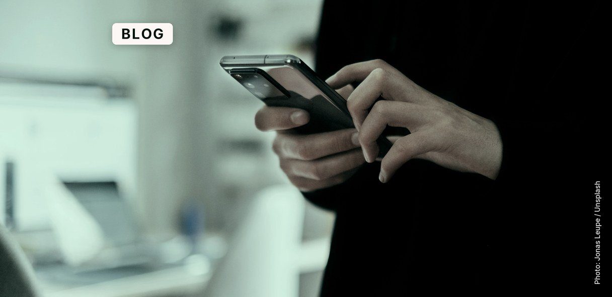 A person holding a black smartphone in one hand